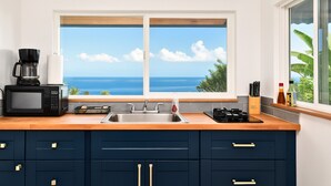 A kitchen with a view of the ocean, a coffee maker, a microwave, a sink, and cabinets.
