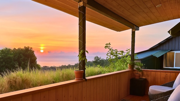 A wooden deck with a view of the sunset, a wicker chair, and a potted plant.