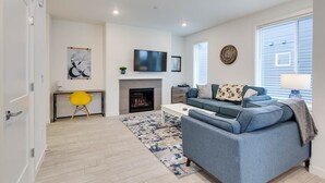 A modern living room with a fireplace, a blue sofa, a yellow chair, and a flat-screen TV.