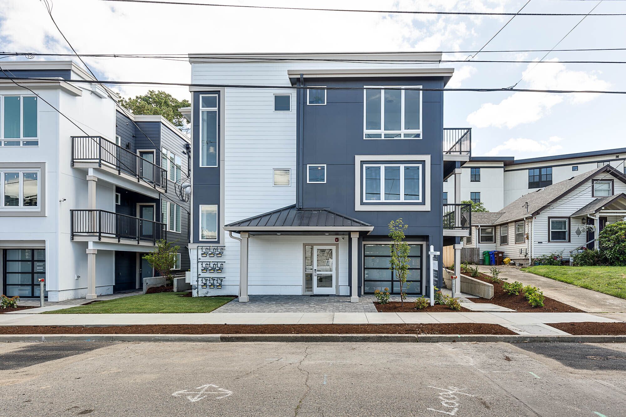 A modern multi-story residential building with a garage entrance, balconies, and a well-maintained lawn.