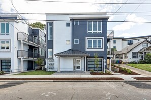 Un immeuble résidentiel moderne à plusieurs étages, doté d’un garage, de balcons et d’une pelouse bien entretenue.