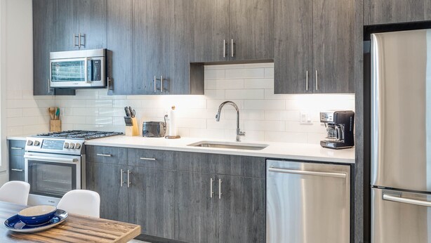 A modern kitchen with dark wood cabinets, stainless steel appliances, and a white tiled backsplash.