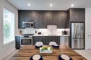 Une cuisine moderne avec des meubles de couleur bois foncé, des appareils en acier inoxydable et une table à manger en bois sur laquelle sont disposées des assiettes bleues.