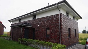 A modern two-story house with a brick facade, a small attached garage, and a paved driveway. - House Spich, Germany (Wittmund)