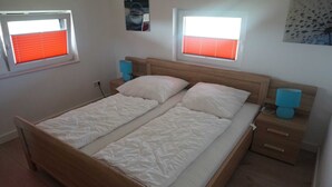 A double bed with a wooden headboard, two bedside tables with lamps, and two windows with red blinds. - House Spich, Germany (Wittmund)