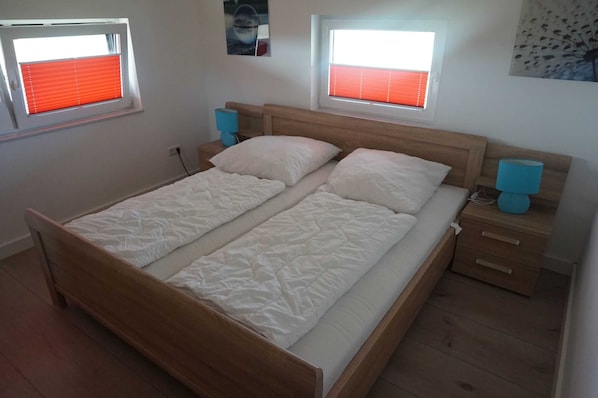 A double bed with a wooden headboard, two bedside tables with lamps, and two windows with red blinds.