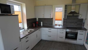 A modern kitchen with white cabinets, a built-in oven, and a microwave. - House Spich, Germany (Wittmund)