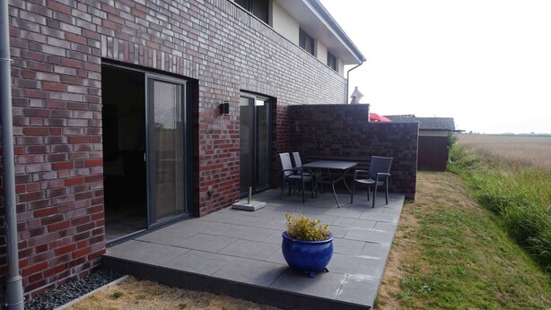 A modern building with a brick exterior, a glass door entrance, and a patio area with outdoor furniture. - House Spich, Germany (Wittmund)