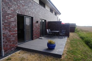A modern building with a brick exterior, a glass door entrance, and a patio area with outdoor furniture.