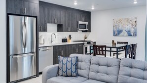 A modern kitchen with dark wood cabinets, stainless steel appliances, and a dining area with a gray sofa and a painting on the wall.