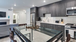 A modern kitchen with dark wood cabinets, stainless steel appliances, and a glass dining table.