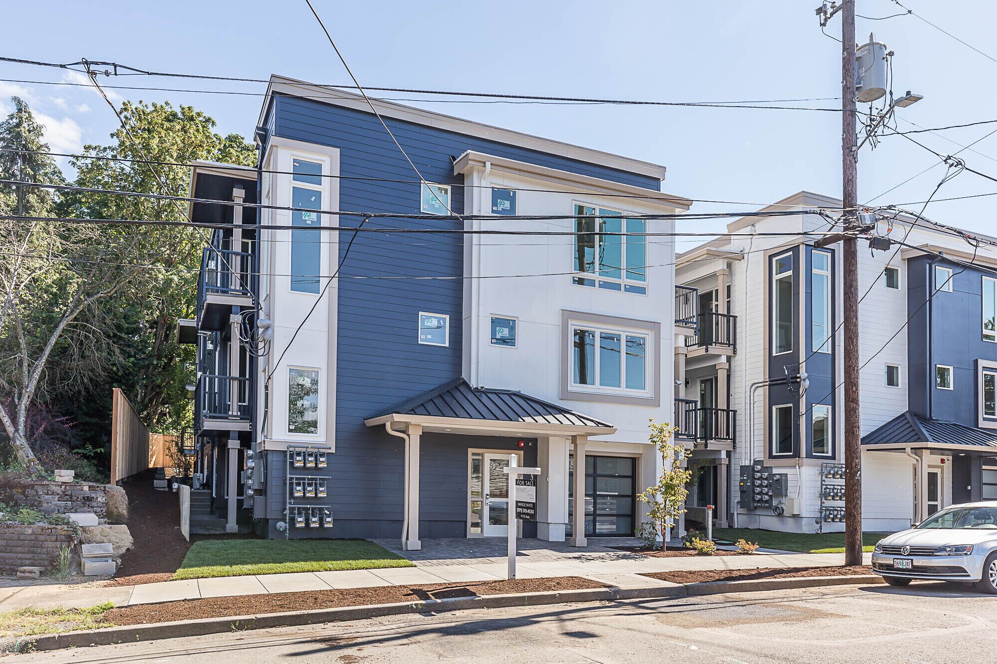 A modern multi-story residential building with a blue exterior, a front entrance, and visible electrical boxes.