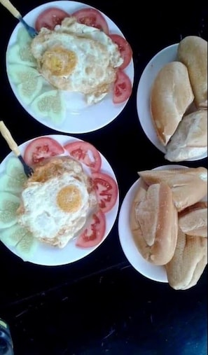 Dos platos con huevos fritos, tomates y pepinos, y un plato con pan.