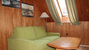 Une pièce avec un canapé vert, une table en bois, des murs en bois, une lampe et une fenêtre avec des rideaux.