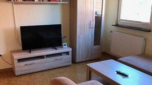 Un salon avec un téléviseur à écran plat posé sur un meuble en bois, un canapé et une table basse.