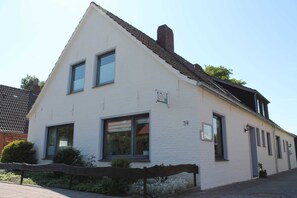 En hvid toetages bygning med gavltag, nummer 34, med store vinduer og et lille haveområde med et træhegn.