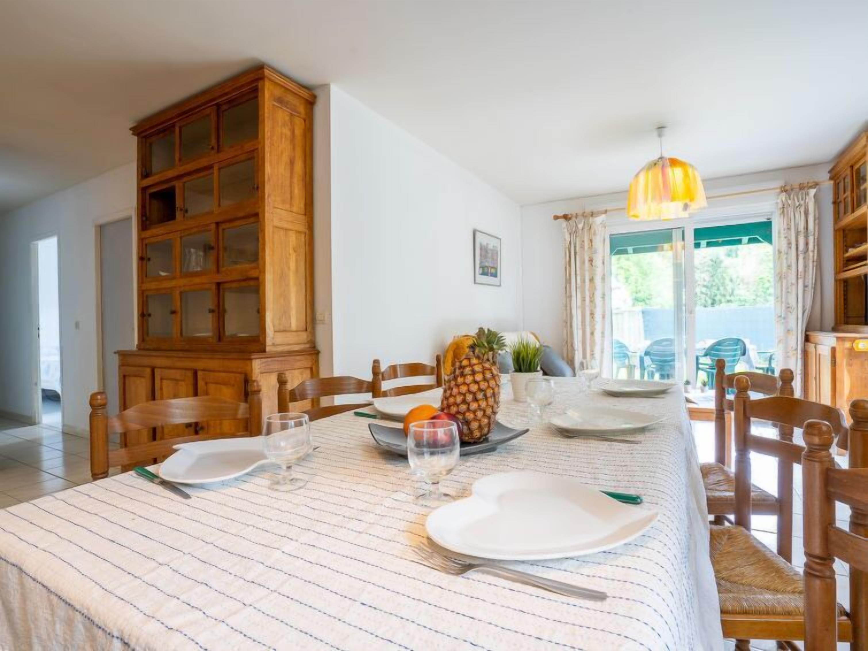 Un coin repas avec une table dressée pour quatre personnes, des chaises en bois, un buffet et une vue sur l’extérieur grâce à une porte vitrée.