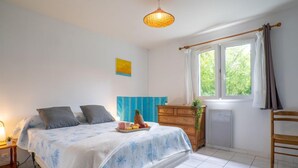 A bedroom with a bed, bedside table, dresser, window, and a hanging light fixture.