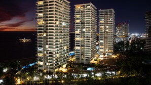 A high-rise hotel with multiple floors, a well-lit pool area, and a view of the surrounding cityscape. - ★ 15th Floor Grand Venetian ★ (Puerto Vallarta)