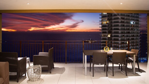 A balcony with wicker furniture, a dining table, and a view of the ocean at sunset. - ★ 15th Floor Grand Venetian ★ (Puerto Vallarta)