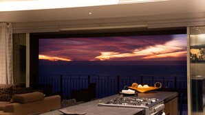 A modern kitchen with a large island, a dining area with a sofa, and a scenic ocean view through a large window. - ★ 15th Floor Grand Venetian ★ (Puerto Vallarta)