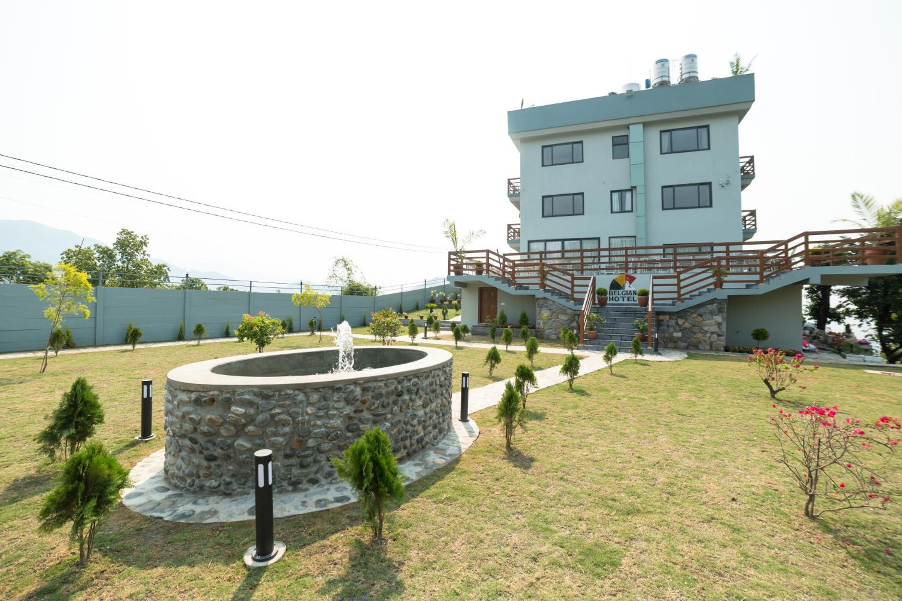 A modern hotel with a stone fountain, a well-maintained lawn, and a balcony with potted plants.