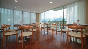 Un comedor amplio con mesas y sillas de madera, y ventanas grandes que ofrecen vistas al exterior.