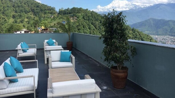 Terraza en la azotea con sillones blancos y cojines azules, con vistas a un paisaje montañoso y una vista de un pueblo más abajo.
