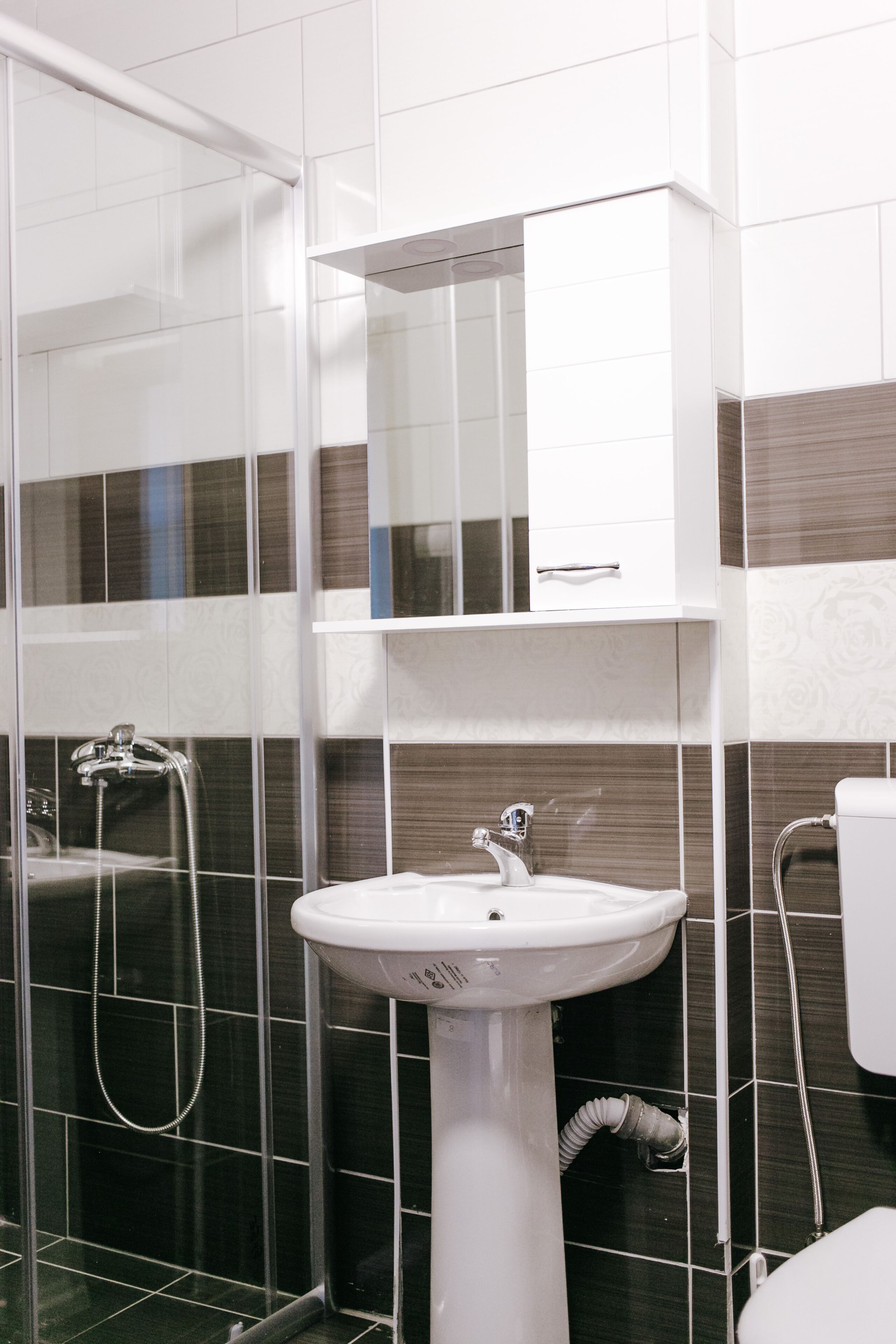 A bathroom with a white pedestal sink, a mirror cabinet, and a shower enclosure.