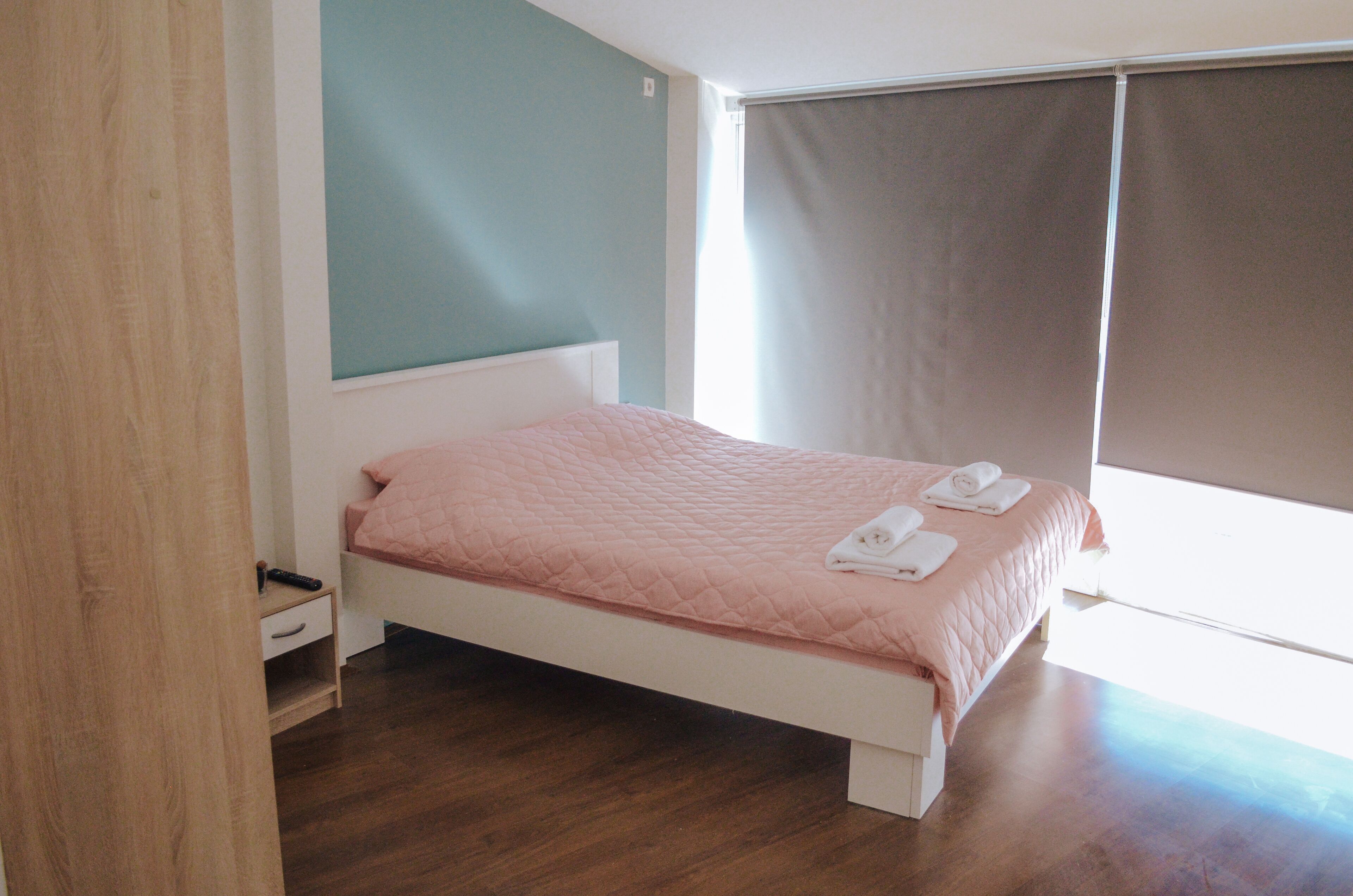 A bedroom with a bed, a bedside table, a window with curtains, and a wooden floor.