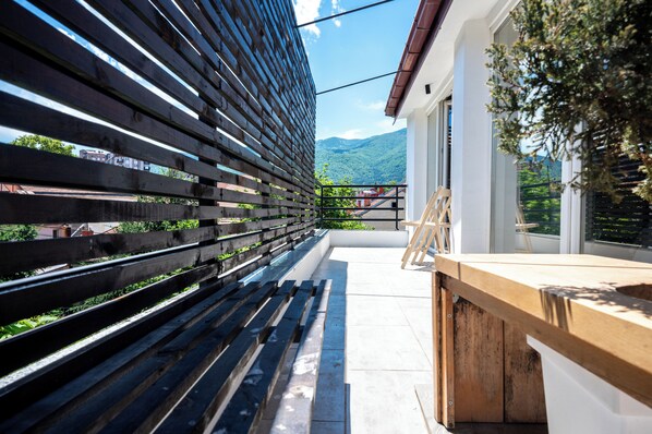 Un balcón con barandilla de madera, una mesa de madera y vistas a un paisaje montañoso.