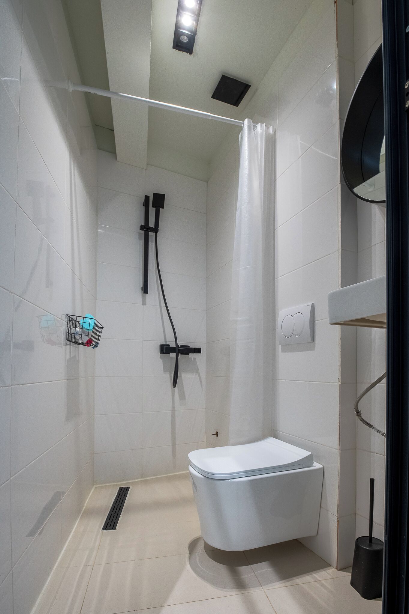 Une salle de bain moderne équipée d’une douche, de toilettes et d’une petite étagère où sont rangés les articles de toilette.