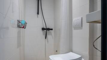 Une salle de bain moderne équipée d’une douche, de toilettes et d’une petite étagère où sont rangés les articles de toilette.