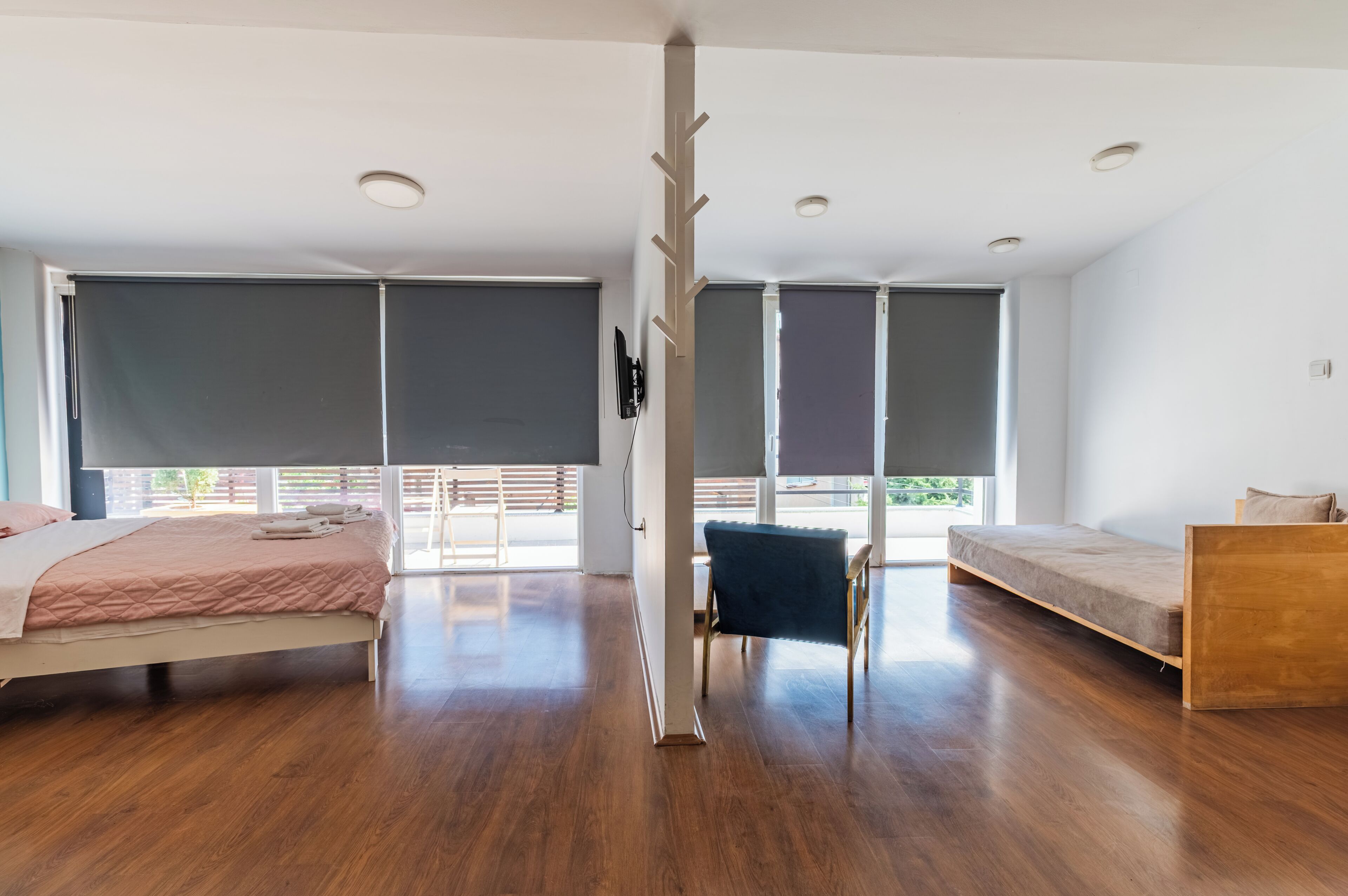 A modern room with a bed, a bench, a wooden structure, and large windows.