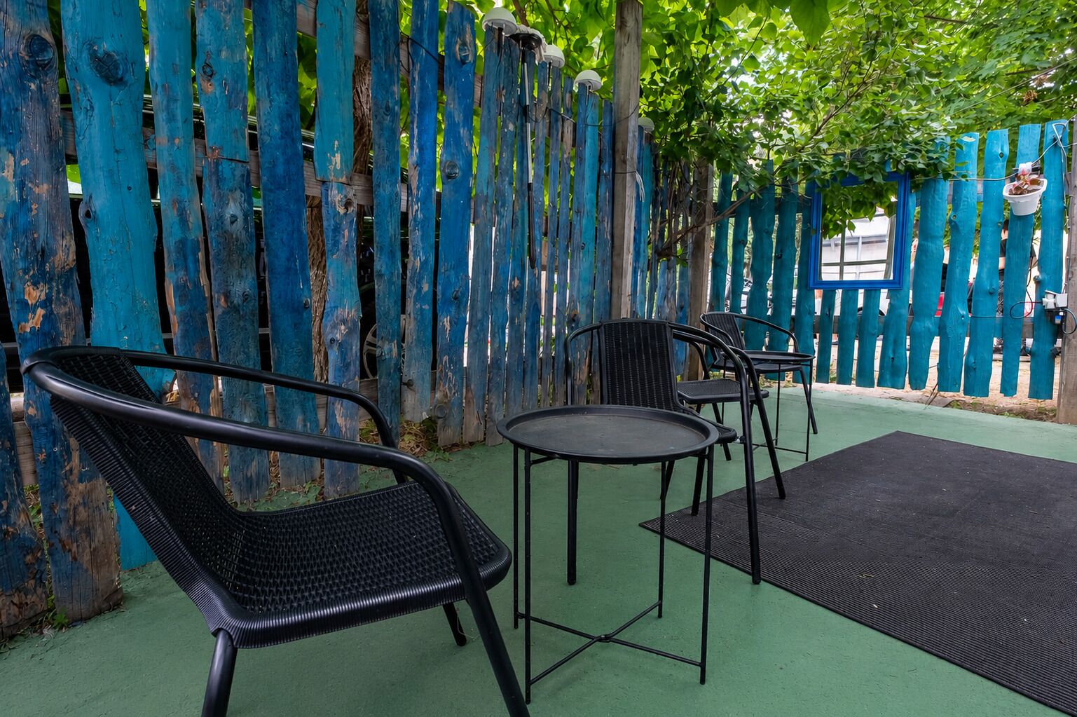 Een terras met buitenmeubilair, zoals stoelen en een tafel, voor een blauwe houten schutting.