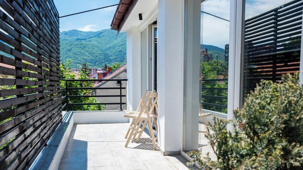 A modern balcony with a wooden bench, a small table, and a potted plant. - White and Wood Boutique Hotel (Bitola)