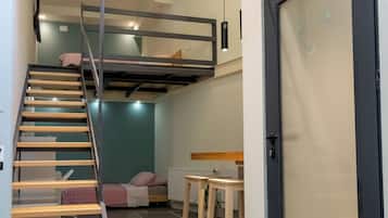 Een ruimtelijk ingerichte leefruimte met een stapelbed, een trap, een eethoek en een deur.