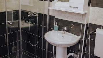 Un baño con cabina de ducha de vidrio, lavamanos sobrepedal y un inodoro.