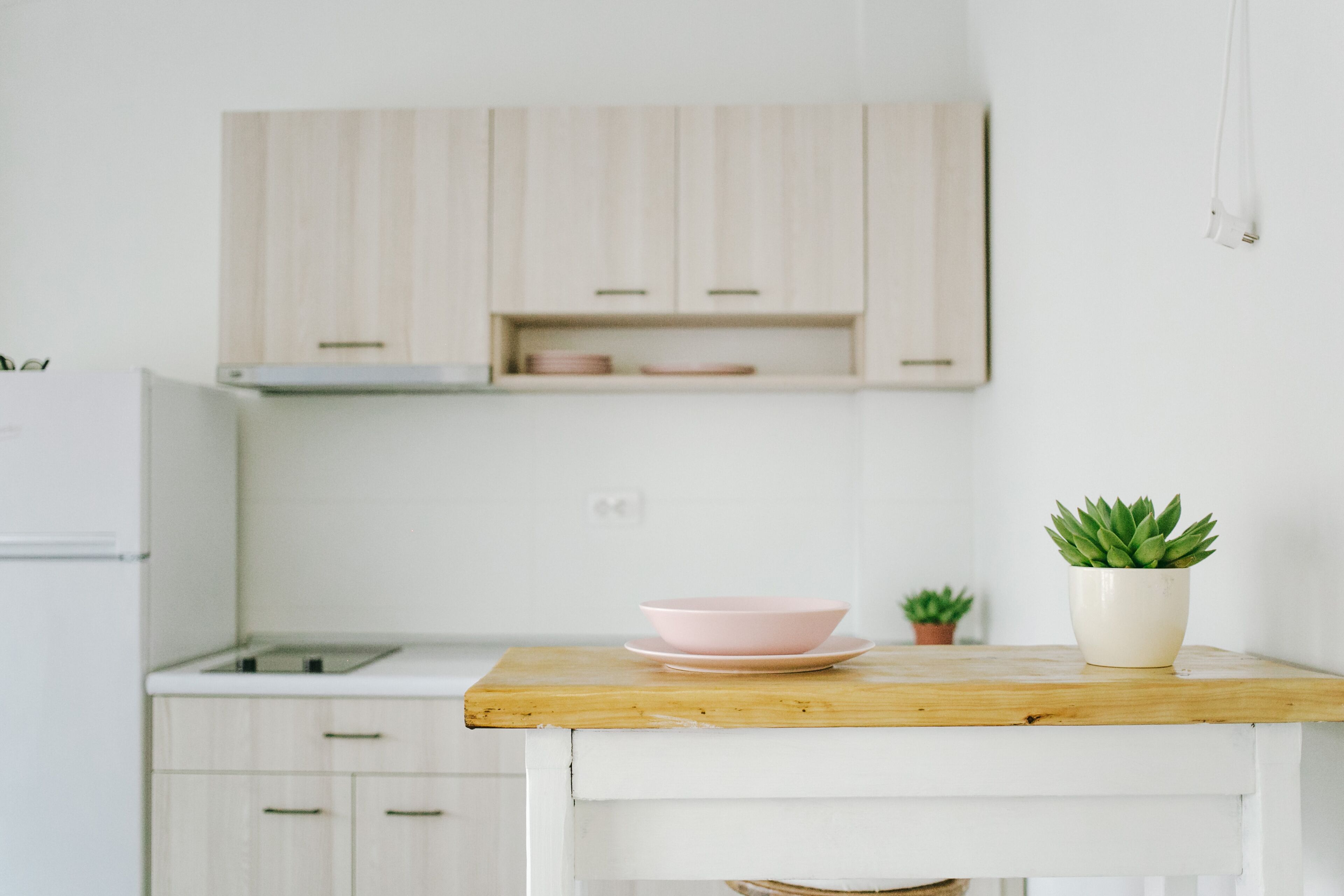 A kitchen with white cabinets, a wooden countertop, a pink bowl, and a small potted plant.