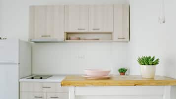 Una cocina con armarios blancos, encimera de madera, un tazón rosa y una pequeña planta en maceta.