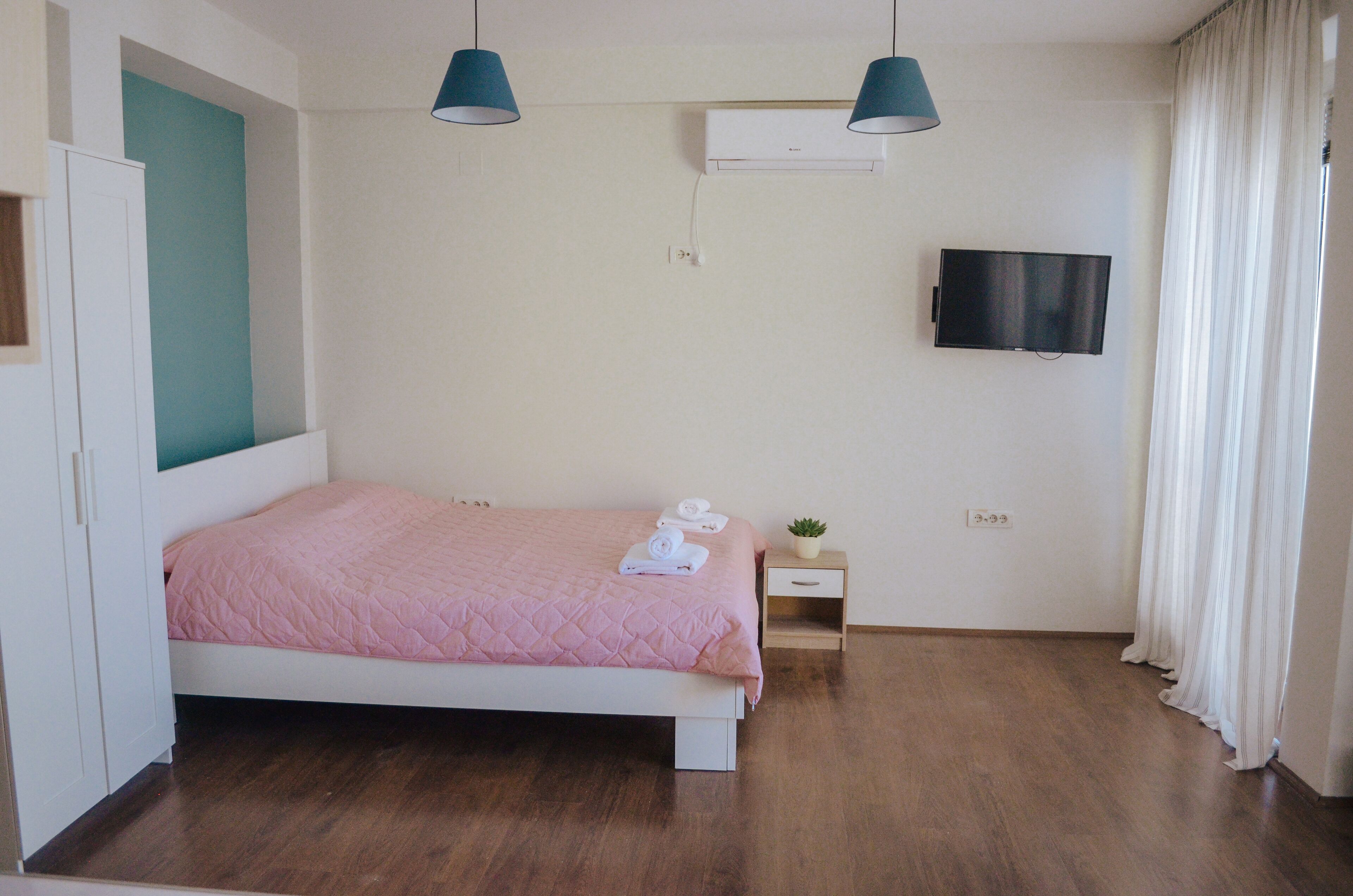 A bedroom with a bed, bedside table, TV, and curtains.