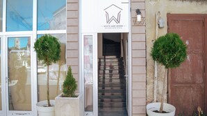 A hotel entrance with a sign reading "WHITE AND WOOD BOUTIQUE HOTEL BITOLA". There are two potted trees in front of the entrance. - White and Wood Boutique Hotel (Bitola)