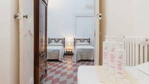 A hotel room with two beds, a checkered floor, and a radiator. There are bottles on a table. - Le Cupole - Andromeda Apartment by Wonderful Italy (Ostuni)