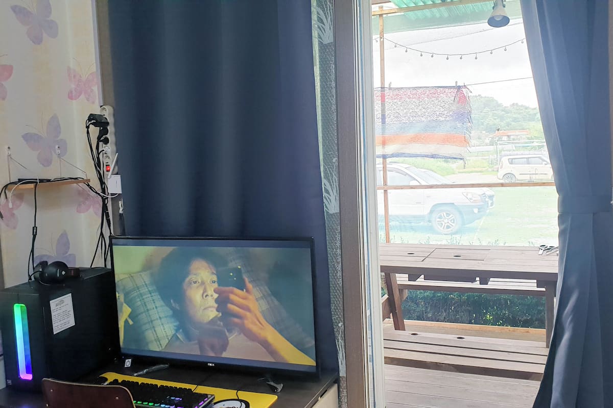 A room with a television on a desk, a computer, and a window with curtains.