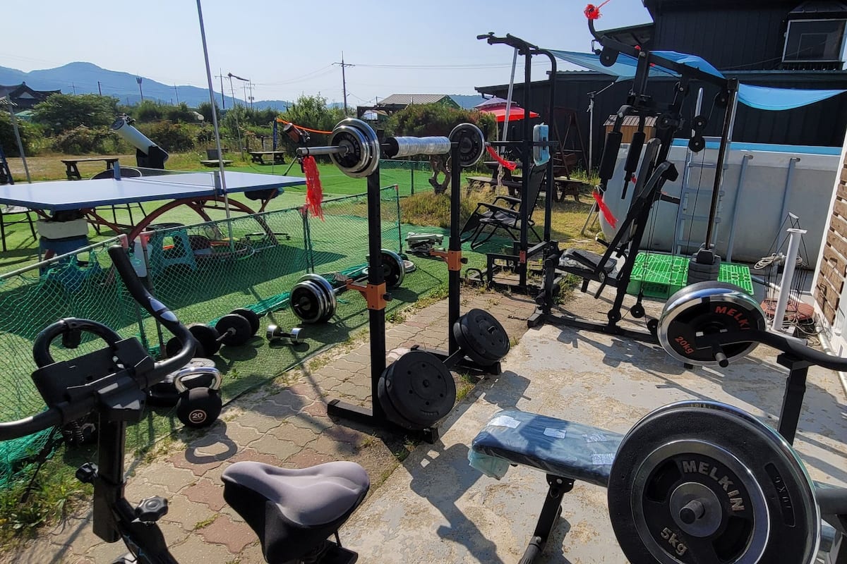 An outdoor gym with various exercise equipment, including a bench press, dumbbells, and weight plates.