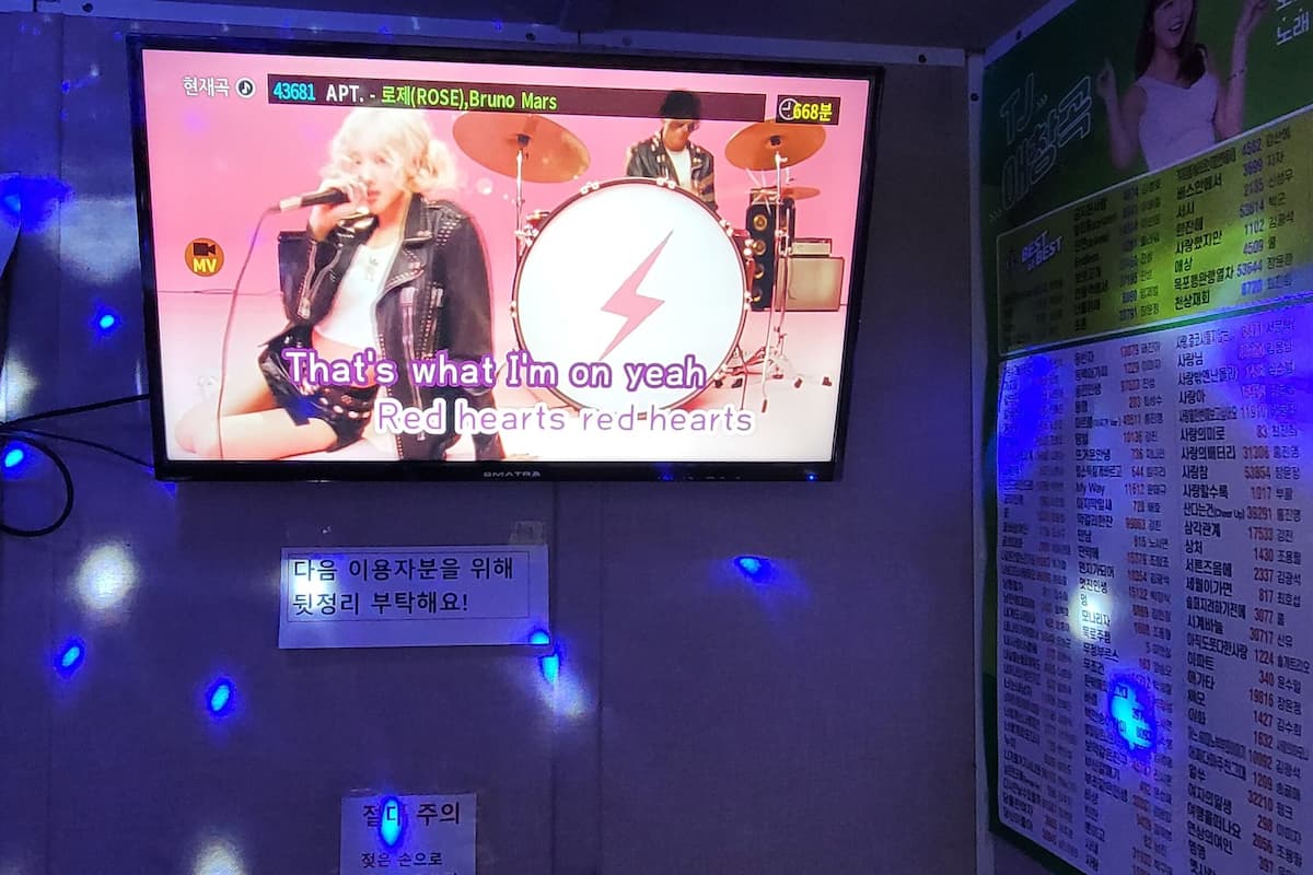 A karaoke room with a screen displaying a song and lyrics, a sound system, and a seating area with blue lights.
