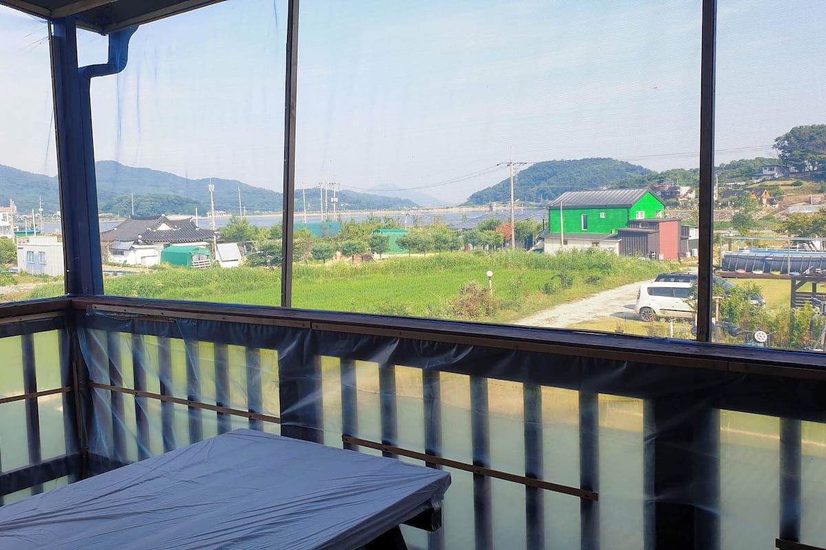 A room with a view of a green house, solar panels, and a distant mountain.