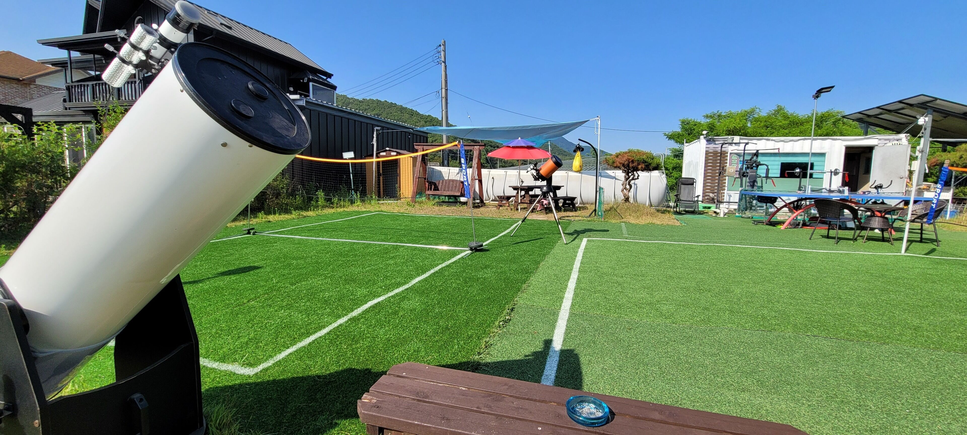 Un telescopio en un campo de césped con una mesa de picnic y un edificio pequeño al fondo.
