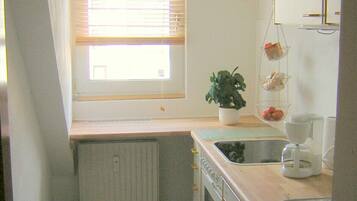 A small kitchen with a window, a radiator, a sink, and a coffee maker.