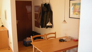 Un'area pranzo con un tavolo e sedie in legno, un attaccapanni con giacche, una porta e un quadro appeso al muro.